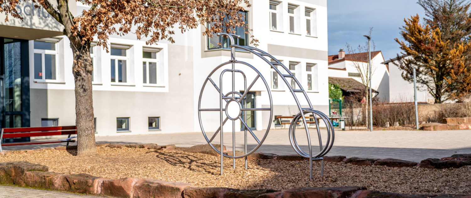 Klettergerüst aus Edelstahl in Form eines antiken Hochrads vor dem Schulgebäude Klettergerüst aus Edelstahl in Form eines antiken Hochrads vor dem Schulgebäude