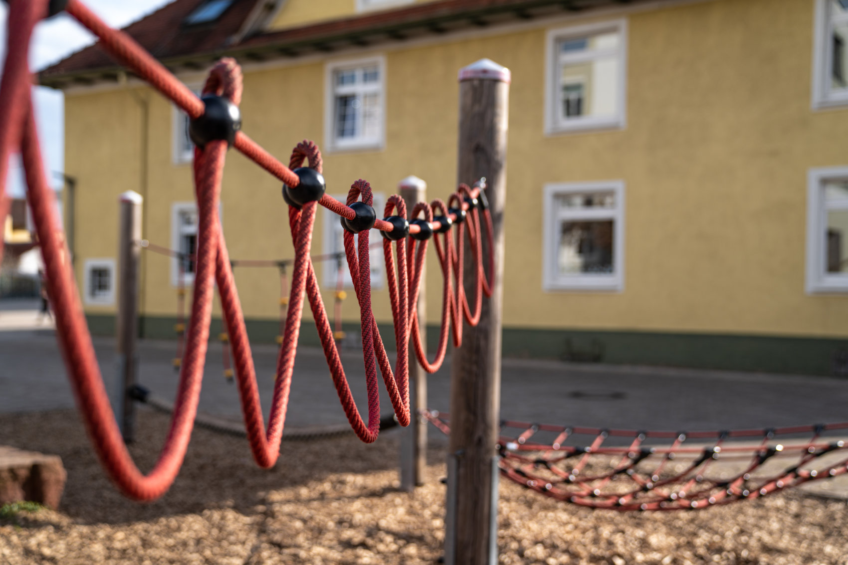 Rote Kletterseile zwischen Holzpfosten mit dem alten Lehrerwohnhaus im Hintergrund Rote Kletterseile zwischen Holzpfosten mit dem alten Lehrerwohnhaus im Hintergrund