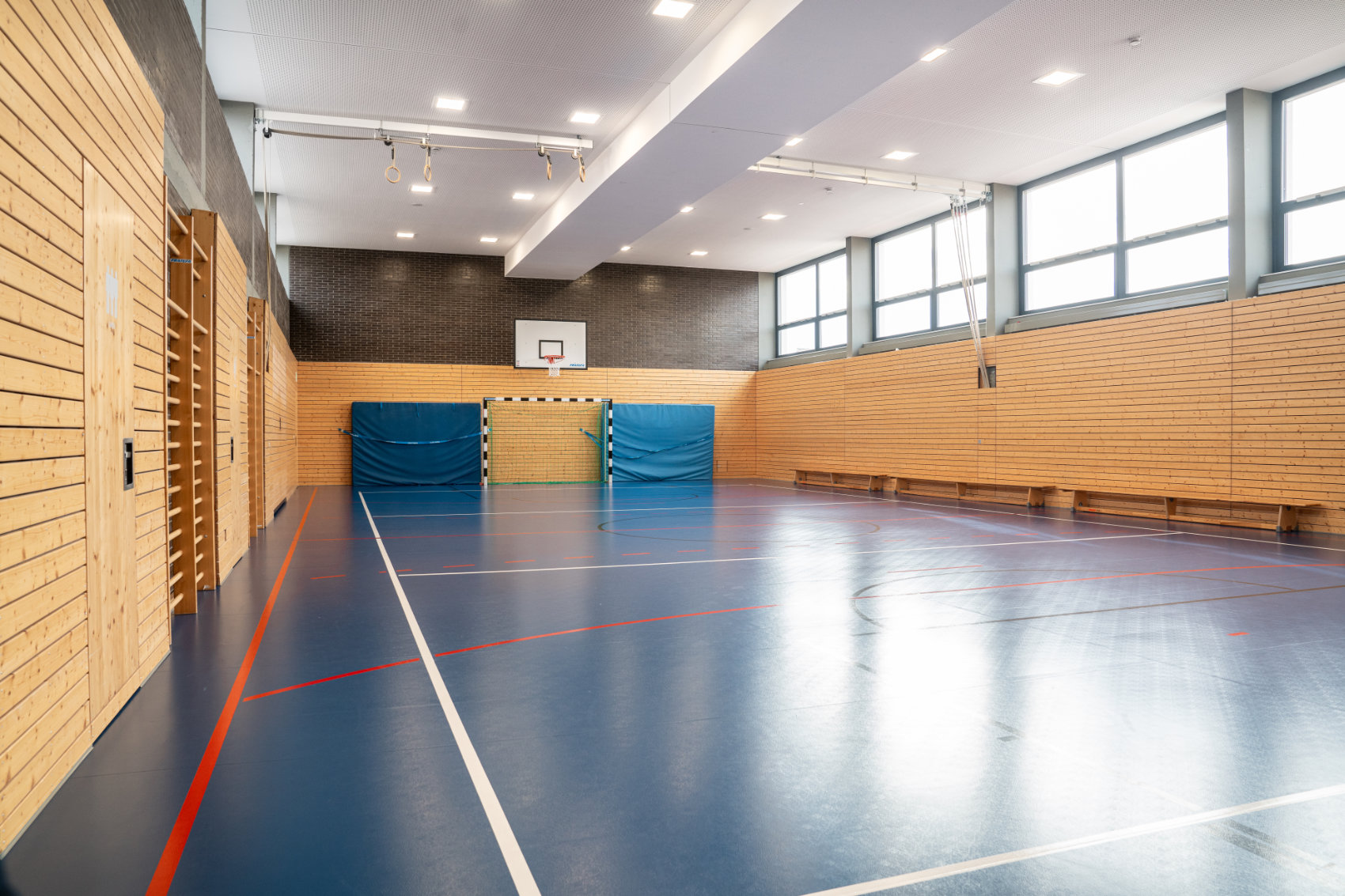 Sporthalle mit blauem Boden und holzverkleideten Wänden 1 Sporthalle mit blauem Boden und holzverkleideten Wänden 1